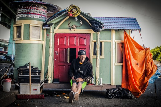 Brian Devlin relaxes on the front porch of his tiny home next to Highway 101 in San Francisco. (Photo by Ekevara Kitpowsong/ Bay News Rising)