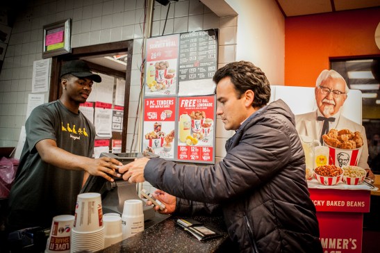 (L-R) A cashier Kelii Agee receives the food order from Homero Hidalgo, 35, part time postmates courier who placing order at KFC/Taco Bell on Duboce Avenue for the customer who requested delivery through the Postmates app on Friday, July 17, 2015. (Photo by Ekevara Kitpowsong/Bay News Rising)