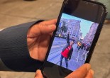 Two hands hold a smartphone, which displays an image of a man holding up his fist on a city street